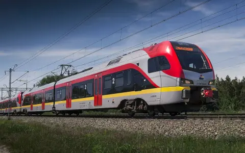 Nowoczesny pociąg do Łodzi mknie po torach wśród zieleni.