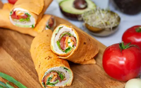 Pyszna tortilla na śniadanie z warzywami i kremowym serkiem. Obok pomidory, awokado i kiełki.