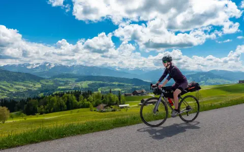 Frau fährt mit Bikepacking-Ausrüstung auf einer Straße mit Alpenpanorama.