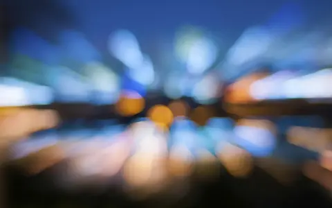 Effetto **vedere sfocato con occhiali nuovi**, luci urbane che si espandono in un caleidoscopio di colori blu e arancio.