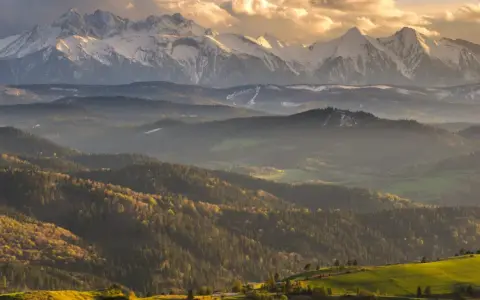 Złote światło oświetla najpiękniejsze szczyty w Polsce, Tatry, otoczone przez malownicze, zalesione wzgórza.