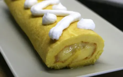 Un brazo de gitano amarillo con relleno cremoso y merengue blanco decorando la superficie.