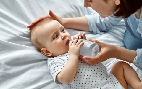 Maluch szarpie się przy karmieniu butelką, ale mama cierpliwie go uspokaja.