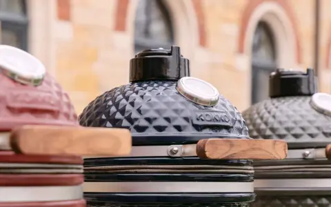 Trois barbecues kamado de couleurs différentes, prêts pour un avis. Le noir est au centre, le rouge à gauche, le gris à droite.