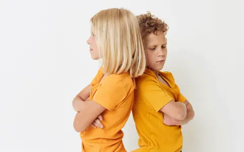 Zwei Kinder stehen mit verschränkten Armen Rücken an Rücken. Ihre Mimik deutet auf **Gewalt unter Geschwistern** hin, ein Streit, der sie trennt.