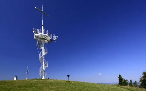 Wieża widokowa na górze Grzywackiej z krzyżem i spiralnymi schodami, na tle błękitnego nieba.