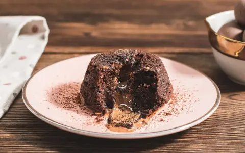 Coulant de chocolate con centro líquido y cremoso, espolvoreado con cacao en polvo sobre un plato rosa.