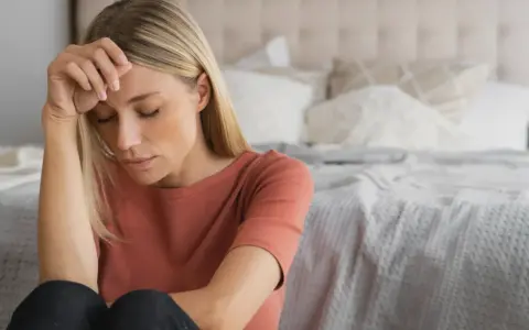 Kvinna med slutna ögon, handen mot pannan. Kanske en känsla av depression under klimakteriet, men det finns behandling.