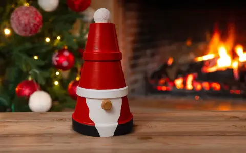 En söt tomte gjord av krukor står framför en sprakande brasa och en julgran. Perfekt för att måla tomte-pyssel.
