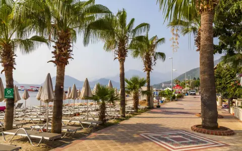 Alejka z palmami prowadzi do plaży w Marmaris, Turcja. Leżaki i parasole czekają na turystów.