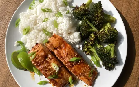 Två saftiga filéer av asiatisk lax serveras med fluffigt ris, rostad broccoli och limeklyftor.