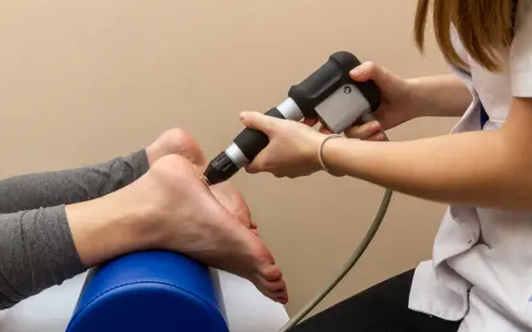 Fizjoterapeuta stosuje terapię falą uderzeniową na stopę pacjentki, by złagodzić ból.