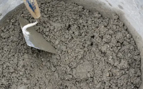 Una cazzuola mescola la malta appena preparata in un secchio. Ecco come fare la malta per i tuoi progetti.