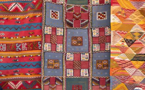 Bunte Teppiche mit geometrischen Mustern, die das orientalische Flair widerspiegeln. Ein Teppich zeigt Streifen, ein anderer Quadrate und das dritte Rauten.