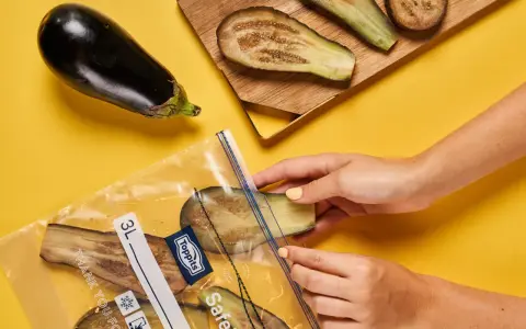 Hände legen Auberginenscheiben in einen Gefrierbeutel. So einfach ist das Aubergine einfrieren für später.