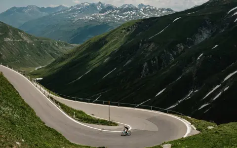 Radfahrer auf einem Transalp Rennrad meistert Serpentinen in den Alpen. Majestätische Bergkulisse mit Schneefeldern.