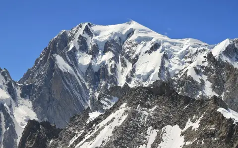 Majestatyczny, ośnieżony szczyt, gdzie jest Mont Blanc, góruje nad skalistym, pokrytym śniegiem zboczem.