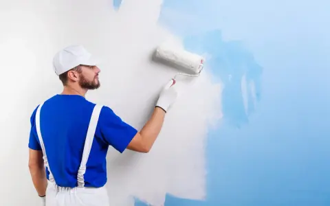 Un peintre en bleu et blanc applique une nouvelle couche de peinture bleue sur un mur blanc. C'est une peinture sur peinture en cours.