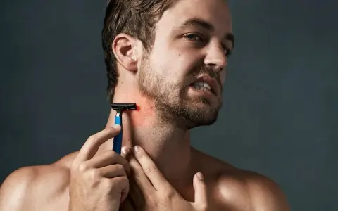 Hombre con piel irritada afeitado, se rasca el cuello con una navaja de afeitar azul.