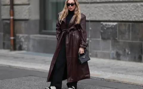 Frau in braunem Leder-Trenchcoat und schwarzen Hosen. Die Frage, welche Farbe passt zu schwarz, wird hier elegant beantwortet: Braun und Schwarz sind ein tolles Duo.