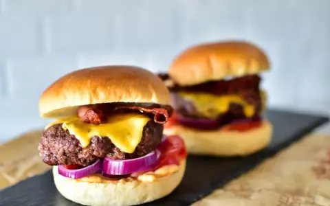 Zwei saftige Burger im Airfryer zubereitet, mit geschmolzenem Käse, knusprigem Speck und roten Zwiebeln.