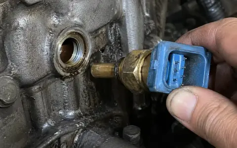 Błąd czujnik temperatury płynu chłodzącego. Mechanik wymienia uszkodzony czujnik w silniku.