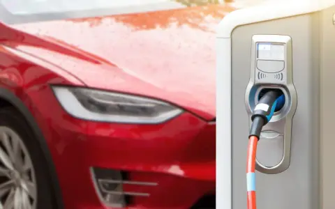 Czerwona Tesla podłączona do ładowarki. Czas ładowania zależy od modelu i mocy stacji.