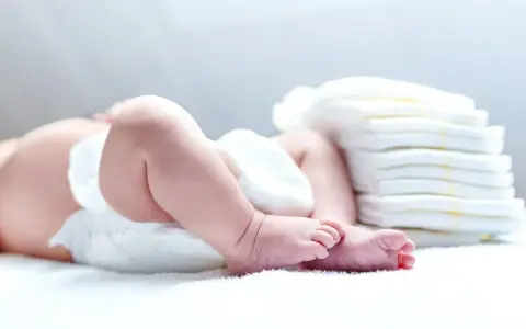 Nietolerancja laktozy u niemowlaka? Śluz w kupie może być sygnałem. Na zdjęciu nóżki dziecka i stos pieluch.