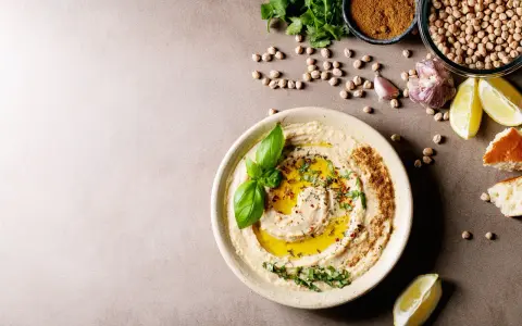 Pyszny hummus z oliwą, ziołami i bazylią. Obok ciecierzyca, czosnek, cytryna i chleb. Czy można mrozić hummus? Tak, można go mrozić.