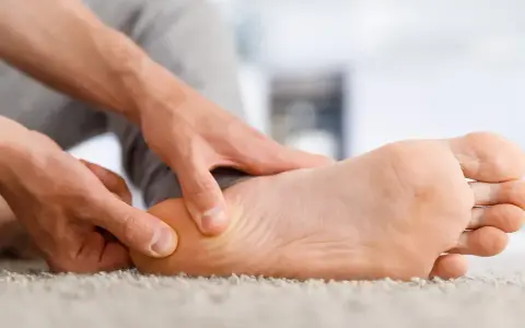 Main d'un homme massant son talon, soulageant une douleur liée à une épine calcanéenne prise en charge.