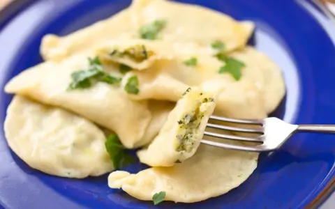 Pyszne pierogi ze szpinakiem, polane masłem i posypane natką pietruszki, czekają na widelcu.