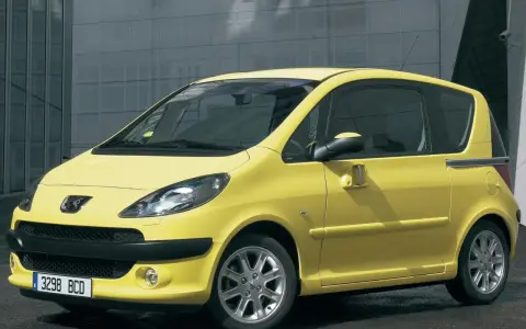Żółty Peugeot 1007 z przesuwnymi drzwiami stoi przed nowoczesnym budynkiem.