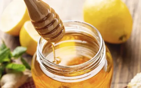 Un pot de miel doré, des citrons et de la menthe, évoquant le bienfait du miel sur la peau.