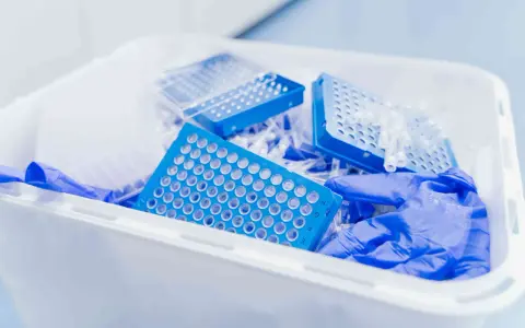 Niebieskie płytki do pipetowania i rękawiczki w pojemniku na odpady laboratoryjne. Kod odpadu 16 03 04.