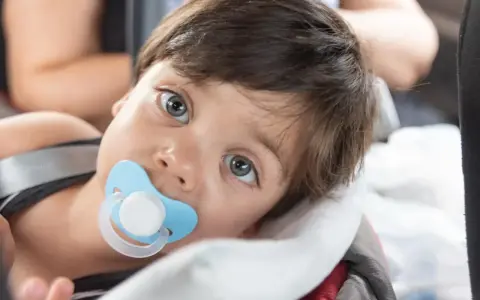 Małe dziecko z niebieskim smoczkiem Tommee Tippee w buzi, zapatrzone w dal.