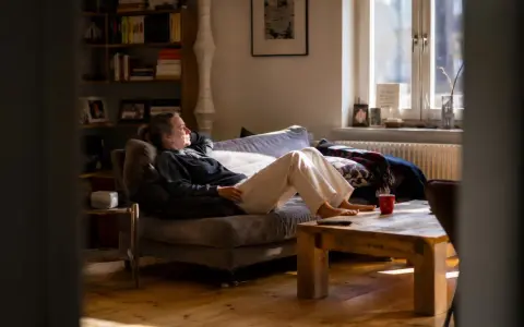 Frau liegt auf Sofa, genießt stille Meditation im warmen Sonnenlicht. Ein Moment der Ruhe im gemütlichen Wohnzimmer.