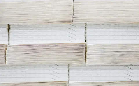 Grandes pilas de papel offset, algunas con finas líneas impresas, apiladas ordenadamente en un almacén.