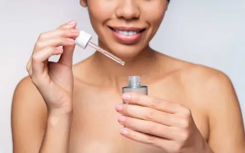 Une femme souriante applique un sérum. Elle se demande combien de temps entre sérum et crème pour une peau parfaite.
