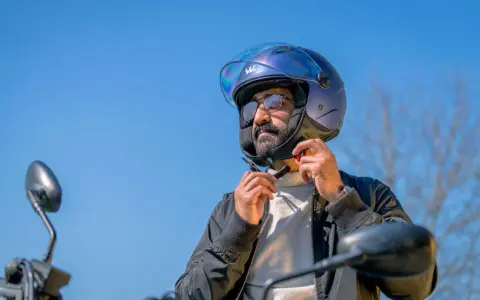Uomo con barba che indossa un casco da moto blu iridescente, pronto per un giro.