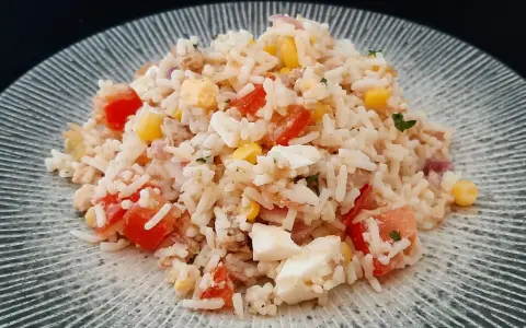 Salade de riz, thon, tomates, maïs et œuf dur sur une assiette grise.
