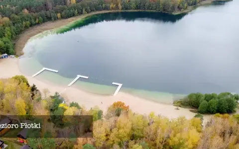 Jesioro Płotki jesienią. Piękna plaża, drewniane pomosty i kolorowe drzewa otaczają spokojną taflę wody.