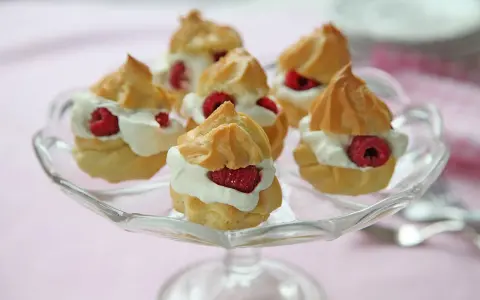 Små petit choux fyllda med grädde och hallon på ett glasfat.