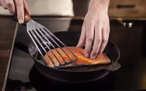 Ein Lachsfilet wird mit einem Pfannenwender in eine heiße Pfanne gelegt. Perfekt für leckere Fisch Rezepte!
