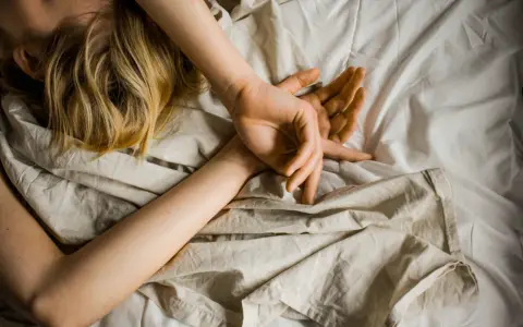 Blonde Haare auf einem Kissen, Arme schlafen nachts ein, Hände ruhen auf der Decke.