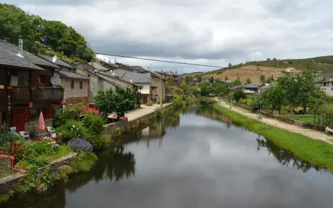 Casas de piedra a orillas del **río de Onor**, con vegetación exuberante y un cielo nublado.