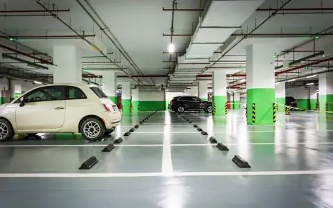 Jasny samochód i ciemny SUV stoją na parkingu podziemnym. Widać wyraźnie wyznaczoną szerokość miejsca parkingowego.