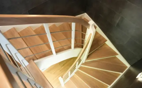 Drewniane schody kacze z białymi balustradami i metalowymi poręczami, prowadzące w dół.