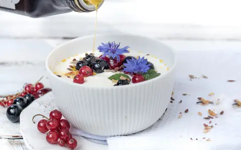 Joghurt mit Beeren und leinsamen, beträufelt mit Honig. Blaue Kornblumen zieren die Schüssel.