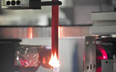A red acrylic rod is tested for how acrylic fire resistant it is, with a flame licking its base.