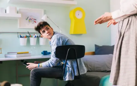 Nastolatek z telefonem w ręku, słuchający rodzica. Czyżby przypominano mu o obowiązkach 16 latka w domu?
